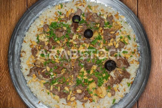 لحم الإبل مع الأرز، طبق رئيسي من المطبخ العربي التقليدي، يُقدم كغداء في مطعم مع اللوز وبذور الصنوبر.