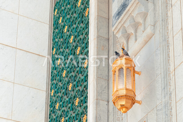 صورة ابداعية لفانوس ذهبي اللون معلق  على جدار المسجد النبوي في المدينه المنوره، التصميم العربي السعودي، ديكورات وزخارف اسلامية
