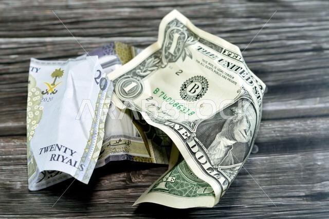 عملة سعودية مجعدة ومتكسرة من فئة 20 ريالاً سعودياً ودولار أمريكي واحد، تضخم العملة وفقدان قيمتها، مفهوم الانخفاض.