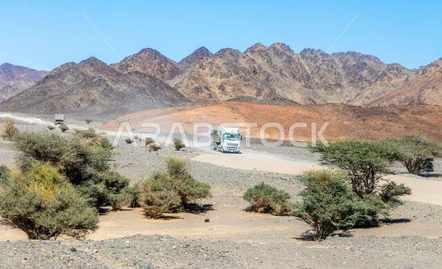 شاحنات في منظر صحراوي مع جبال في الخلفية، بالقرب من العلا، المملكة العربية السعودية