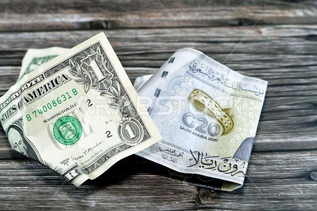 عملة سعودية مجعدة ومتكسرة من فئة 20 ريالاً سعودياً ودولار أمريكي واحد، تضخم العملة وفقدان قيمتها، مفهوم الانخفاض.