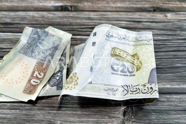ورقة نقدية مصرية مجعدة من فئة 20 جنيهاً مصرياً، وورقة نقدية سعودية من فئة 20 ريالاً سعودياً عليها شعار قمة مجموعة العشرين، وأوراق نقدية مجعدة، وأوراق نقدية سعودية ومصرية