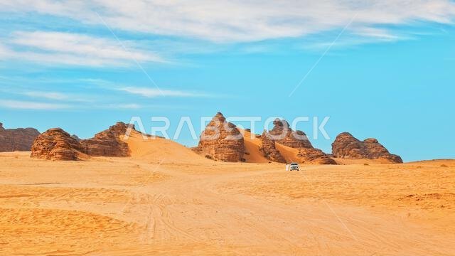 Typical desert landscape in Alula, Saudi Arabia, sand with some mountains, small offroad vehicle, local man and camels at distance