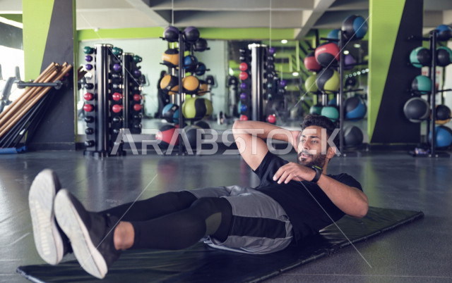 A Saudi Arabian Gulf youth doing exercises on a yoga mat, strengthening health and bodies, exercising in the gym