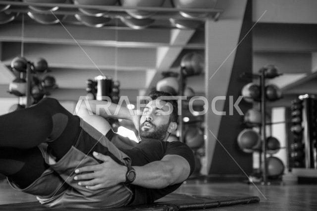 شاب عربي خليجي سعودي يقوم بتمارين الرياضية على سجادة اليوغا ، تقوية الصحة و الأجسام ، ممارسة التمارين الرياضية في النادي الرياضي