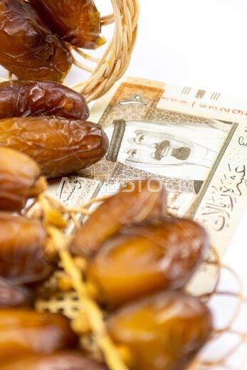 صورة مقرّبة لتمور جزائرية ملكية على طبق خشبي. عملات ورقية سعودية. مفهوم رمضان.