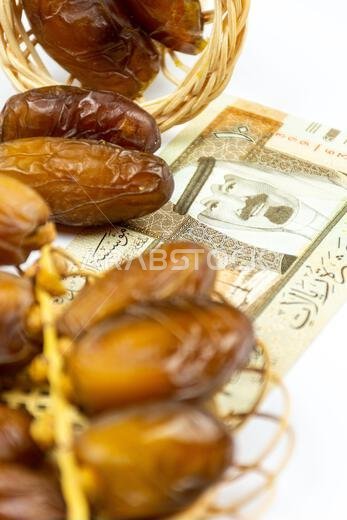 صورة مقرّبة لتمور جزائرية ملكية على طبق خشبي. عملات ورقية سعودية. مفهوم رمضان.