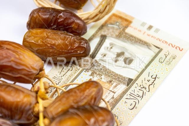 صورة مقرّبة لتمور جزائرية ملكية على طبق خشبي. عملات ورقية سعودية. مفهوم رمضان.