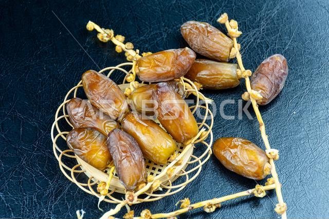 صورة مقرّبة لتمور جزائرية ملكية على طبق خشبي على خلفية سوداء. مفهوم رمضان.