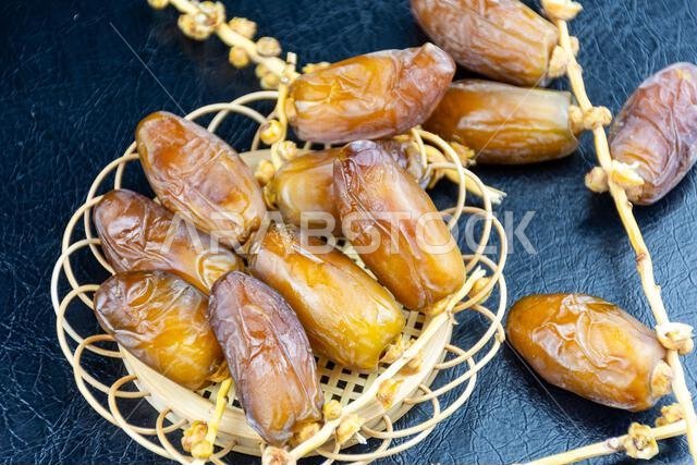 صورة مقرّبة لتمور جزائرية ملكية على طبق خشبي على خلفية سوداء. مفهوم رمضان.