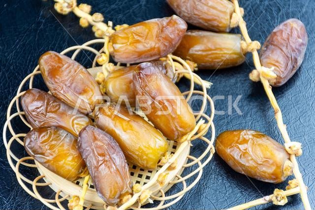 صورة مقرّبة لتمور جزائرية ملكية على طبق خشبي على خلفية سوداء. مفهوم رمضان.