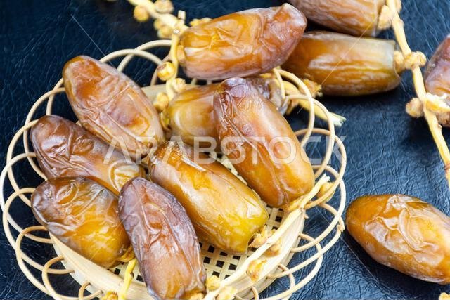 Close-up of Algerian royal dates on a wooden plate on a black background. Ramadan concept.