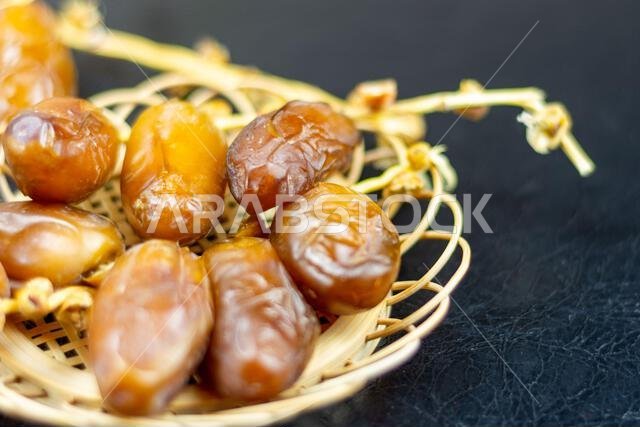 Close-up of Algerian royal dates on a wooden plate on a black background. Ramadan concept.