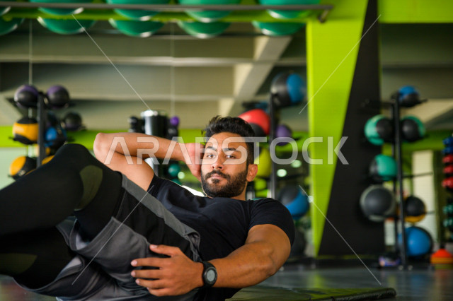 شاب عربي خليجي سعودي يقوم بتمارين الرياضية على سجادة اليوغا ، تقوية الصحة و الأجسام ، ممارسة التمارين الرياضية في النادي الرياضي