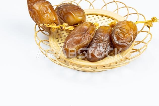 صورة مقرّبة لتمور جزائرية ملكية على طبق خشبي على خلفية بيضاء. مفهوم رمضان.