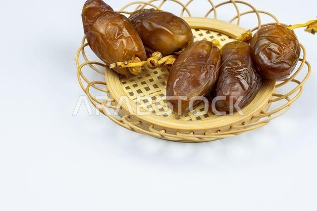 صورة مقرّبة لتمور جزائرية ملكية على طبق خشبي على خلفية بيضاء. مفهوم رمضان.