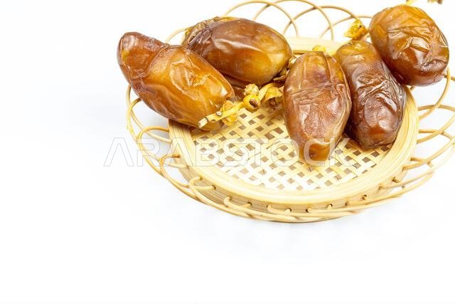 صورة مقرّبة لتمور جزائرية ملكية على طبق خشبي على خلفية بيضاء. مفهوم رمضان.