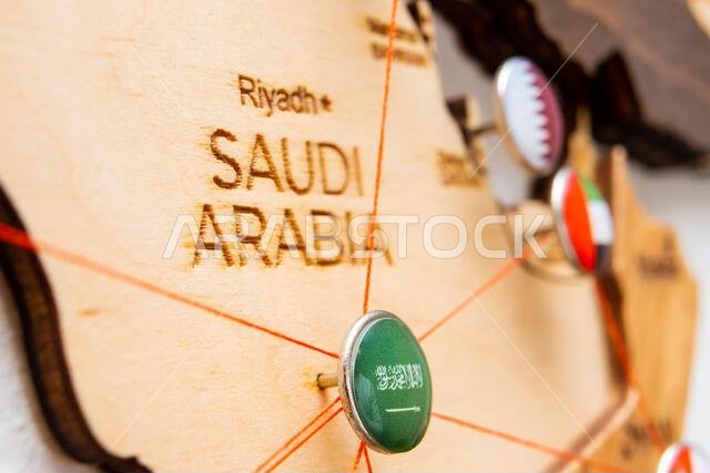 علم المملكة العربية السعودية على دبوس التثبيت وخيوط حمراء على الخريطة الخشبية. طرق السفر أو الخدمات اللوجستية. النفوذ في الجغرافيا السياسية والاقتصاد العالمي. 