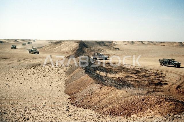 A convoy of M-998 high-mobility, multipurpose, wheeled vehicles drives past a berm as the 4th Battalion, 2nd Brigade move their camp near the border of Iraq during Operation Desert Storm. Subject Operation/Series: DESERT STORM Country: Saudi Arabia(SAU)