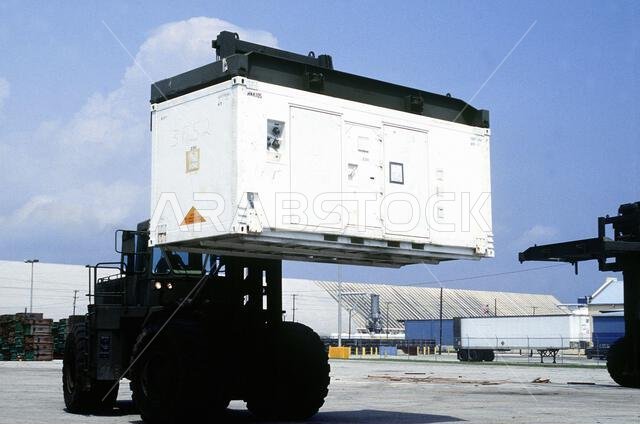 تقوم رافعة شوكية بوضع حاوية/مأوى في منطقة التجميع استعدادًا لشحنها إلى المملكة العربية السعودية دعمًا لعملية درع الصحراء. العملية/السلسلة: درع الصحراء. القاعدة: مورهيد سيتي. الولاية: كارولاينا الشمالية. الدولة: الولايات المتحدة الأمريكية. تقوم رافعة شوكية بوضع حاوية/مأوى في منطقة التجميع استعدادًا لشحنها إلى المملكة العربية السعودية دعمًا لعملية درع الصحراء. العملية/السلسلة: درع الصحراء. القاعدة: مورهيد سيتي. الولاية: كارولاينا الشمالية. الدولة: الولايات المتحدة الأمريكية.