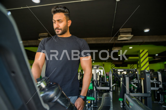 شاب عربي خليجي سعودي يقوم بالتمرن على جهاز المشي ، ممارسة التمارين الرياضية في النادي الرياضي