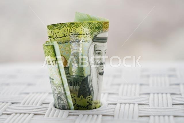لقطة مقرّبة لأوراق نقدية سعودية خضراء، مثبتة على سطح أبيض، تجسد مفهوم الثروة والادخار.