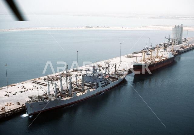 ترسو سفينة الشحن "كيب بون" (T-AK-5059)، المستأجرة من قبل قيادة النقل البحري العسكري، على رصيف الميناء، وقد فُتحت عنابر الشحن استعدادًا لتحميل المعدات والذخائر لإعادة نشرها في الولايات المتحدة في أعقاب عملية عاصفة الصحراء. ترسو سفينة تجارية خلف "كيب بون". العملية/السلسلة: عاصفة الصحراء. الدولة: المملكة العربية السعودية.