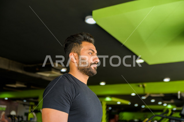 شاب عربي خليجي سعودي يقوم بالتمرن على جهاز المشي ، ممارسة التمارين الرياضية في النادي الرياضي