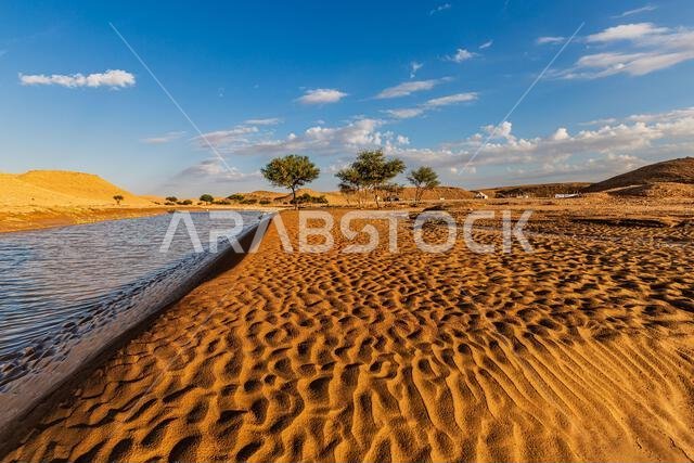 Desert landscape and lake after rain with tents in distance, Saudi Arabia