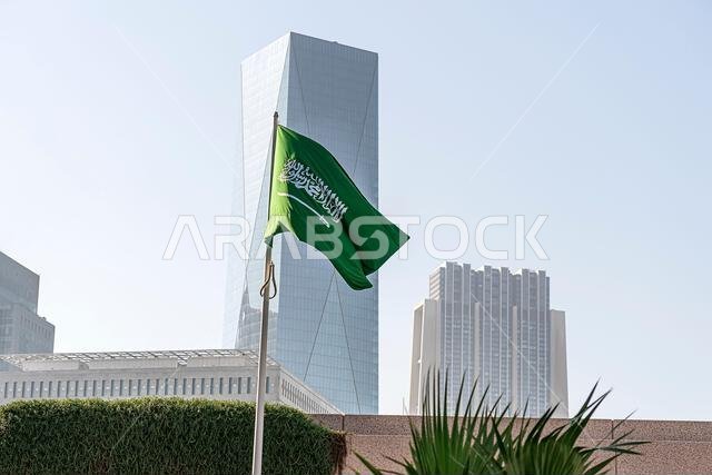 علم المملكة العربية السعودية على خلفية مبنى شاهق،