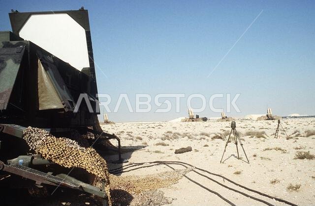 An AN/MPQ-53 radar set, left, for the MIM-104 Patriot tactical air defense system is deployed at a newly constructed site during Operation Desert Shield. The radar set is a multifunction, phased array device which performs surveillance, tracking and guidance functions. In the background are four Patriot launchers.. Subject Operation/Series: DESERT SHIELD Country: Saudi Arabia(SAU)