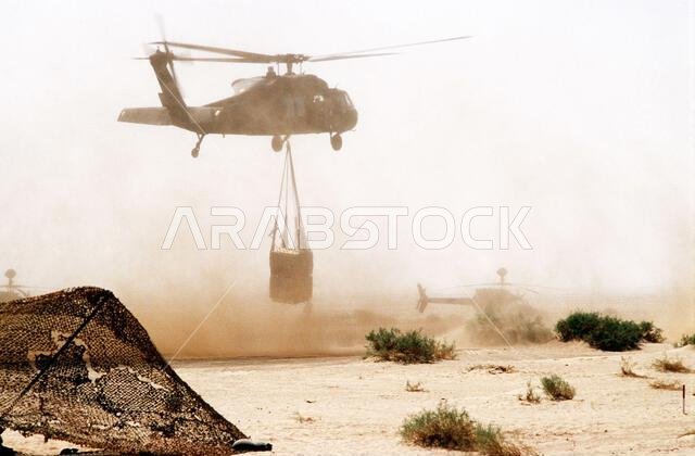 تقوم مروحية من طراز UH-60 بلاك هوك (بلاك هوك) بنقل الإمدادات إلى معسكر قاعدة خلال عملية درع الصحراء. العملية/السلسلة: درع الصحراء. الدولة: المملكة العربية السعودية. تقوم مروحية من طراز UH-60 بلاك هوك (بلاك هوك) بنقل الإمدادات إلى معسكر قاعدة خلال عملية درع الصحراء. العملية/السلسلة: درع الصحراء. الدولة: المملكة العربية السعودية.