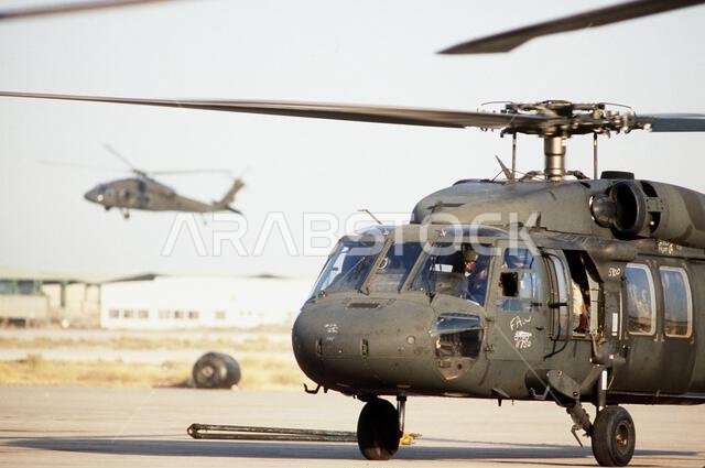تستعد مروحية UH-60A بلاك للإقلاع بينما تمر مروحية بلاك هوك أخرى في الخلفية خلال عملية درع الصحراء. الموضوع: عملية درع الصحراء، الدولة: المملكة العربية السعودية. تستعد مروحية UH-60A بلاك للإقلاع بينما تمر مروحية بلاك هوك أخرى في الخلفية خلال عملية درع الصحراء. الموضوع: عملية درع الصحراء، الدولة: المملكة العربية السعودية.