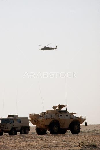 تحلق مروحية من طراز UH-60 بلاك هوك (بلاك هوك) بالقرب من مركبتين عسكريتين سعوديتين خلال عملية درع الصحراء. على اليسار مركبة بينزغاور توربو دي رباعية الدفع؛ وعلى اليمين ناقلة جنود مدرعة من طراز V-150 كوماندو. موضوع العملية/السلسلة: عملية درع الصحراء. الدولة: المملكة العربية السعودية.