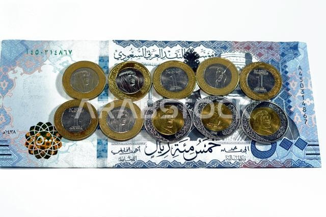 ورقة نقدية من فئة 500 ريال سعودي مع رزمة من العملات المعدنية من فئة ريال واحد وريالين، تحمل صورة الملك سلمان بن عبد العزيز آل سعود. ورقة نقدية من فئة 500 ريال سعودي مع رزمة من العملات المعدنية من فئة ريال واحد وريالين، تحمل صورة الملك سلمان بن عبد العزيز آل سعود.
