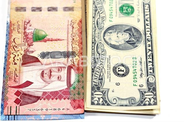 ورقة نقدية من فئة 100 ريال سعودي تحمل صورة الملك سلام والمسجد النبوي، وأخرى من فئة 20 دولاراً أمريكياً تحمل صورة الملك سلام والمسجد النبوي.
