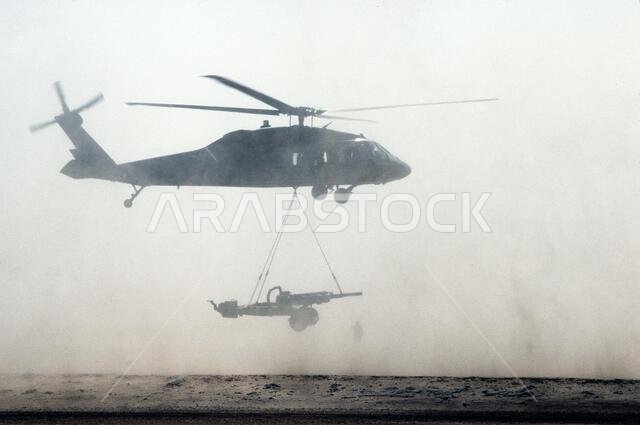 مروحية من طراز UH-60 بلاك هوك (بلاك هوك) ترفع مدفع هاوتزر M-102 عيار 105 ملم خلال عملية درع الصحراء. العملية/السلسلة: درع الصحراء. الدولة: المملكة العربية السعودية.