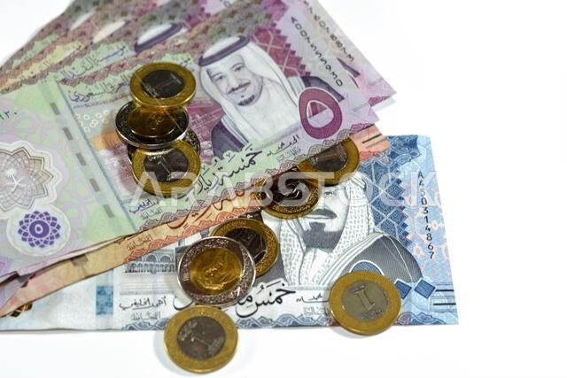 أوراق نقدية وعملات معدنية من الريال السعودي، تتضمن رزمة من فئات 500 و100 و5 ريالات، بالإضافة إلى عملات معدنية من فئتي 1 و2 ريال، تحمل صورة الملك سلمان بن عبد العزيز آل سعود.