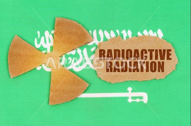 مفهوم الصناعة والإشعاع. على علم المملكة العربية السعودية، رمز النشاط الإشعاعي وقطعة من الورق المقوى الممزق مكتوب عليها "مشع".