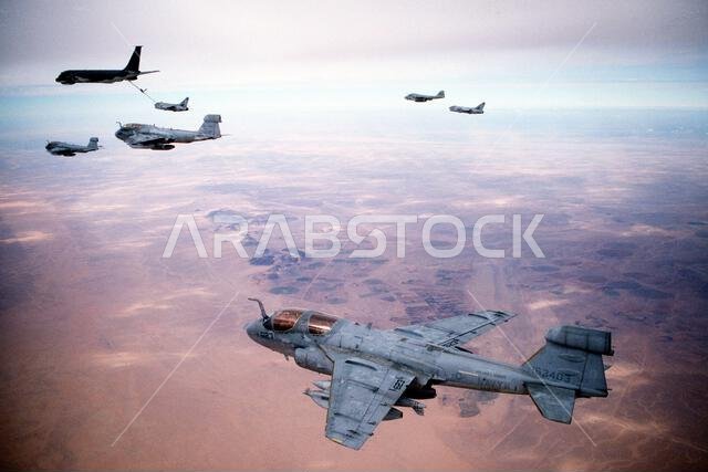 Three Tactical Electronic Warfare Squadron 130 (VAQ-130) EA-6B Prowler aircraft wait as an Attack Squadron 72 (VA-72) A-7E Corsair aircraft is refueled by an Air Force KC-135E Stratotanker aircraft to refuel while en route to targets in Iraq during Operation Desert Storm. At upper right, an Attack Squadron 75 (VA-75) A-6E Intruder aircraft carrying a "buddy store" external fuel tank refuels a second Corsair aircraft. The Navy aircraft are based aboard the aircraft carrier USS JOHN F. KENNEDY (CV