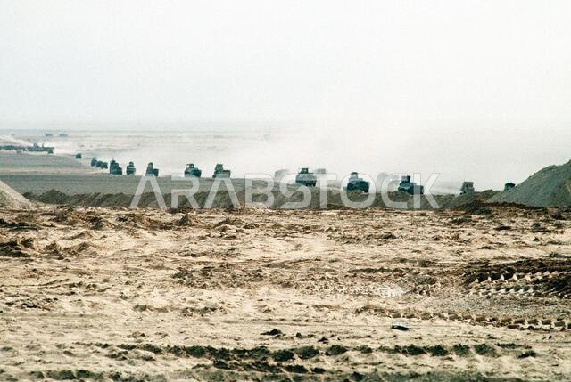 A convoy of heavy vehicles from Naval Mobile Construction Battalion Five (NMCB-5) drives toward a site in northern Saudi Arabia during Operation Desert Storm. Subject Operation/Series: DESERT STORM Country: Saudi Arabia (SAU)