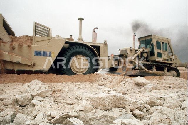 A bulldozer is used to push a motorized earthmoving scraper as Seabees assigned to Naval Mobile Construction Battalion Five (NMCB-5) prepare a camp in northern Saudi Arabia during Operation Desert Storm. Subject Operation/Series: DESERT STORM Country: Saudi Arabia (SAU)