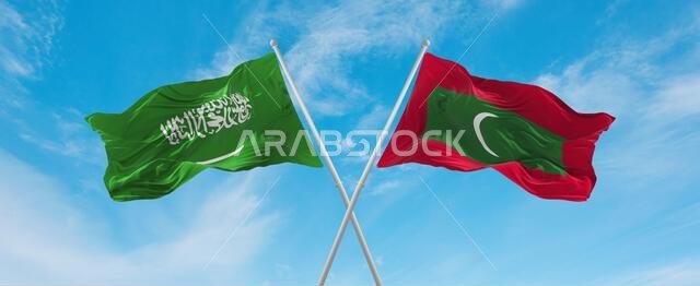 علمان متقاطعان، علم جزر المالديف وعلم المملكة العربية السعودية، يرفرفان في مهب الريح تحت سماء ملبدة بالغيوم. يرمز هذا إلى مفهوم العلاقة والحوار والسفر بين البلدين. رسم توضيحي ثلاثي الأبعاد.