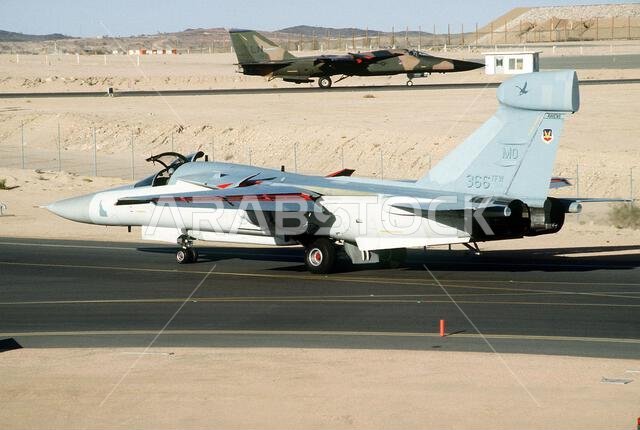 طائرة حرب إلكترونية من طراز EF-111A Raven تابعة للجناح المقاتل التكتيكي 366، قيادة القوات الجوية التكتيكية، تستعد لمهمة خلال عملية درع الصحراء. في الخلفية، طائرة مقاتلة من طراز F-111F تابعة للجناح المقاتل التكتيكي 48، القوات الجوية الأمريكية في أوروبا، تتجه نحو المدرج للإقلاع. الموضوع: عملية/سلسلة: درع الصحراء، الدولة: المملكة العربية السعودية. طائرة حرب إلكترونية من طراز EF-111A Raven تابعة للجناح المقاتل التكتيكي 366، قيادة القوات الجوية التكتيكية، تستعد لمهمة خلال عملية درع الصحراء. في الخلفية، طائرة مقاتلة من طراز F-111F تابعة للجناح المقاتل التكتيكي 48، القوات الجوية الأمريكية في أوروبا، تتجه نحو المدرج للإقلاع. الموضوع: عملية/سلسلة: درع الصحراء، الدولة: المملكة العربية السعودية.