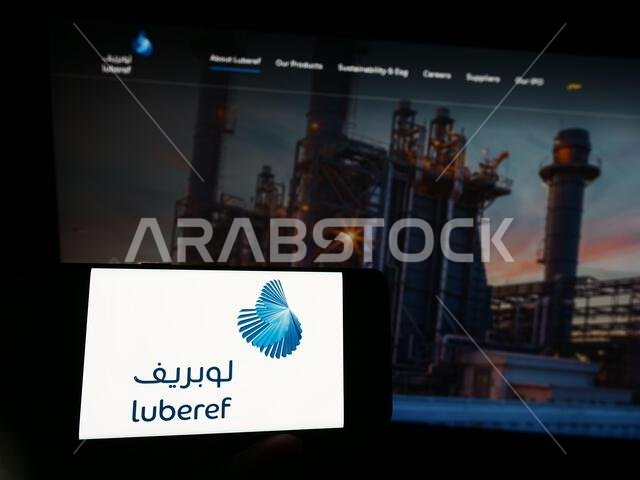 شخص يحمل هاتفًا محمولًا عليه شعار شركة لوبريف السعودية للزيوت الأساسية، أمام صفحة ويب خاصة بالشركة. التركيز على شاشة الهاتف.