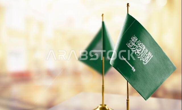 Small flags of the Saudi Arabia on an abstract blurry background.