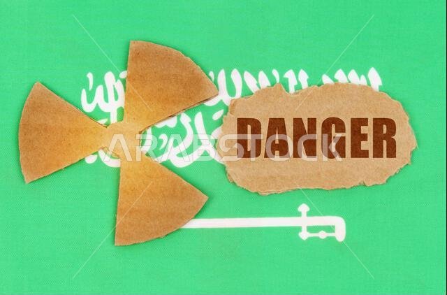 مفهوم الصناعة والإشعاع. على علم المملكة العربية السعودية، رمز النشاط الإشعاعي وقطعة من الورق المقوى الممزق مكتوب عليها: خطر مفهوم الصناعة والإشعاع. على علم المملكة العربية السعودية، رمز النشاط الإشعاعي وقطعة من الورق المقوى الممزق مكتوب عليها: خطر