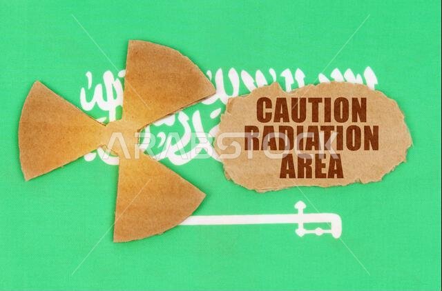 مفهوم الصناعة والإشعاع. على علم المملكة العربية السعودية، رمز النشاط الإشعاعي وقطعة من الورق المقوى الممزق مكتوب عليها: تحذير من الإشعاع