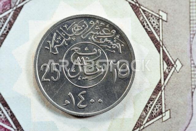 الوجه الخلفي لعملة سعودية قديمة من فئة ربع ريال (25 هلالة، سلسلة 1400 هـ)، مع وجود نقش فوق الكتابة داخل دائرة. الوجه الخلفي لعملة سعودية قديمة من فئة ربع ريال (25 هلالة، سلسلة 1400 هـ)، مع وجود نقش فوق الكتابة داخل دائرة.