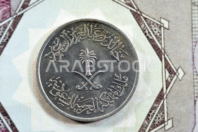 سيفان متقاطعان ونخلة في وسط وجه العملة المعدنية القديمة السعودية ربع ريال سعودي من فئة 25 هلالة، 1400 هـ. سيفان متقاطعان ونخلة في وسط وجه العملة المعدنية القديمة السعودية ربع ريال سعودي من فئة 25 هلالة، 1400 هـ.